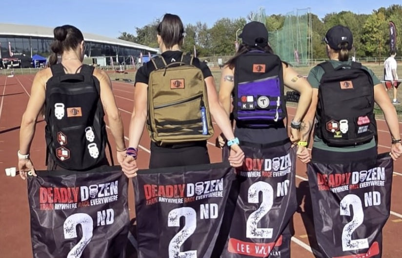 Four athletes wearing YOMP rucking backpacks holding Deadly Dozen 2nd place flags at Deadly Dozen Lee Valley